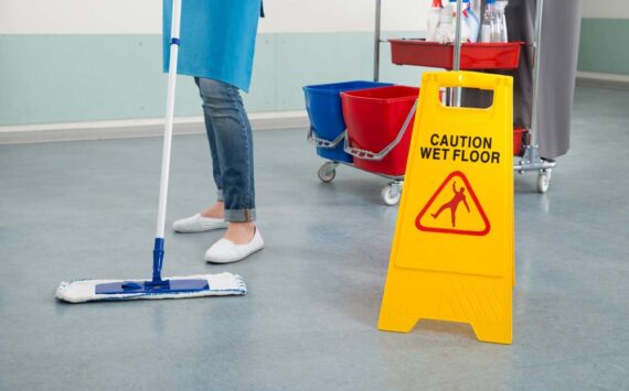 person mopping a floor and a yellow caution wet floor sign